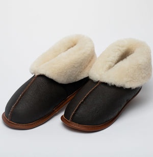A close up shot on a white background of a very nice pair of brown Ithaca Sheepskin Slippers with the cuffs folded down, exposing the cream colored fur lining.